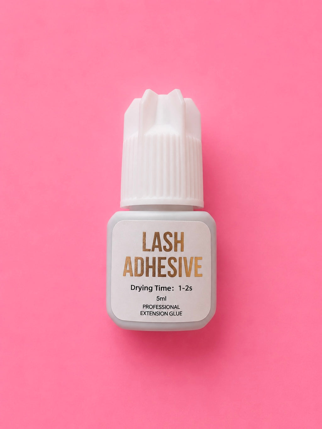 A small bottle of lash adhesive with a white cap and white label, featuring gold text, centred on a solid pink background.1-2 Seconds Fast Clear Lash Extension Adhesive Glue Bratty Beauty XO