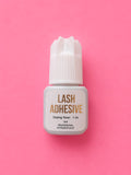 A small bottle of lash adhesive with a white cap and white label, featuring gold text, centred on a solid pink background.1-2 Seconds Fast Clear Lash Extension Adhesive Glue Bratty Beauty XO