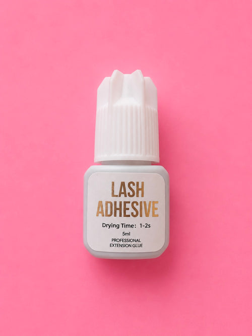 A small bottle of lash adhesive with a white cap and white label, featuring gold text, centred on a solid pink background.1-2 Seconds Fast Clear Lash Extension Adhesive Glue Bratty Beauty XO