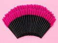 A fan arrangement of black and hot pink makeup spoolie brushes on a solid pink background.100 or 300 pcs | Disposable Lash Spoolies for Eyelash Extensions Bratty Beauty XO