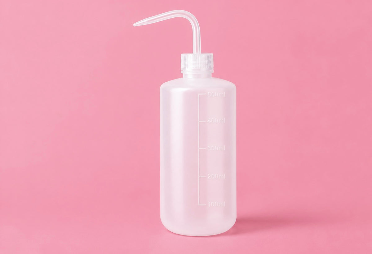 A translucent white plastic wash bottle with a clear curved spout and measurement markings, set against a solid pink background250ml or 500ml Pink/White Tattoo Wash Bottle Bratty Beauty XO