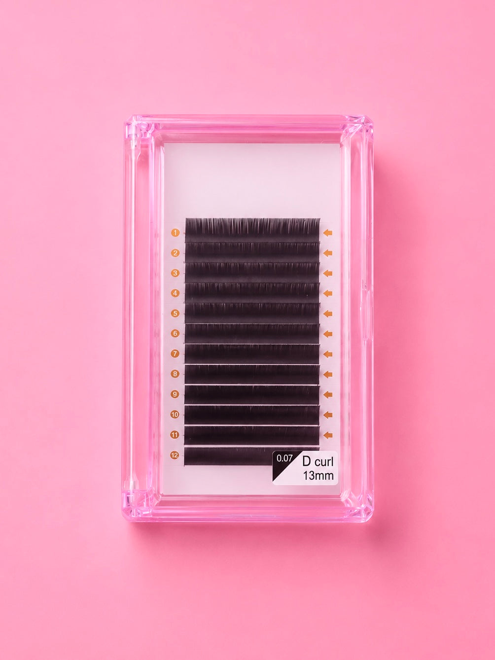 A pack of black false eyelashes with a D curl, presented in a clear pink plastic case on a solid pink background.Bratty Beauty XO Matte Black 0.07 D Curl 13mm Lash Extension Tray