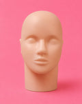 A realistic bald mannequin head with closed eyes, displayed on a matching neck stand against a solid pink background. this product is for beginner lash artist to practice on.Lash Practice Mannequin Head Bratty Beauty XO