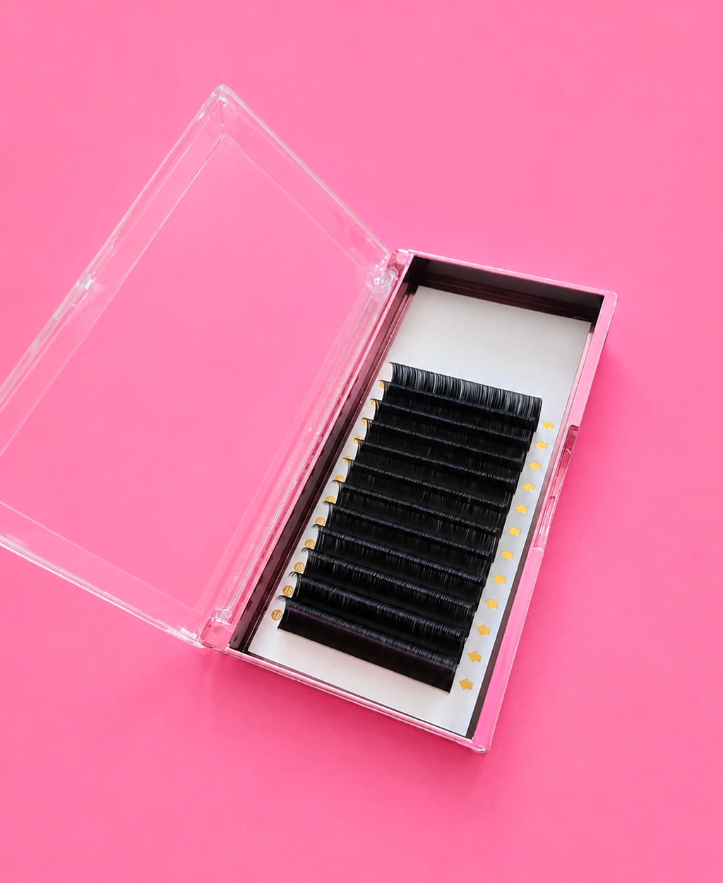 A clear plastic case opened to reveal black false eyelashes arranged in rows on a white insert, set against a solid pink background.Matte Black 0.5D Curl 14mm Lash Extension Tray Bratty Beauty XO