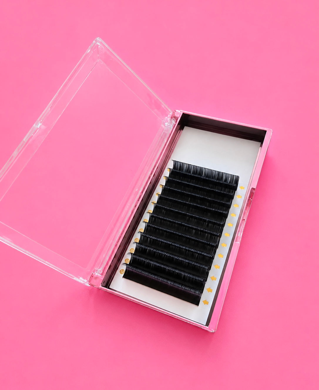 A clear plastic case opened to reveal black false eyelashes arranged in rows on a white insert, set against a solid pink background.Matte Black 0.5D Curl 14mm Lash Extension Tray Bratty Beauty XO