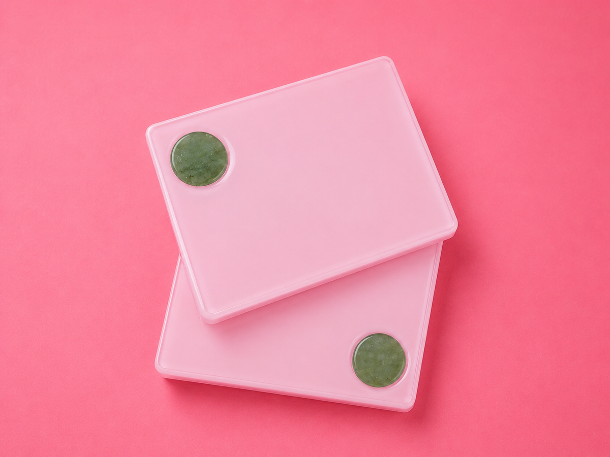 Two light pink rectangular plastic cases with circular green accents, stacked diagonally on a solid pink background.Rosie Pink Acrylic Lash Tile Bratty Beauty XO