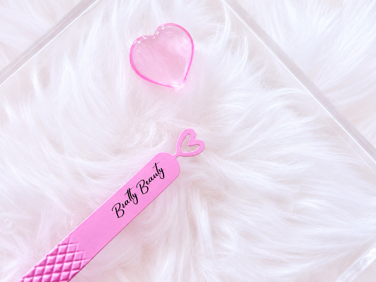 Pink beauty tool set featuring a long spatula labeled 'Butty Beauty' and a small heart-shaped container, displayed on a white faux fur surface.Big Boss Fanning Tweezer, bratty beauty xo volume lash tweezer