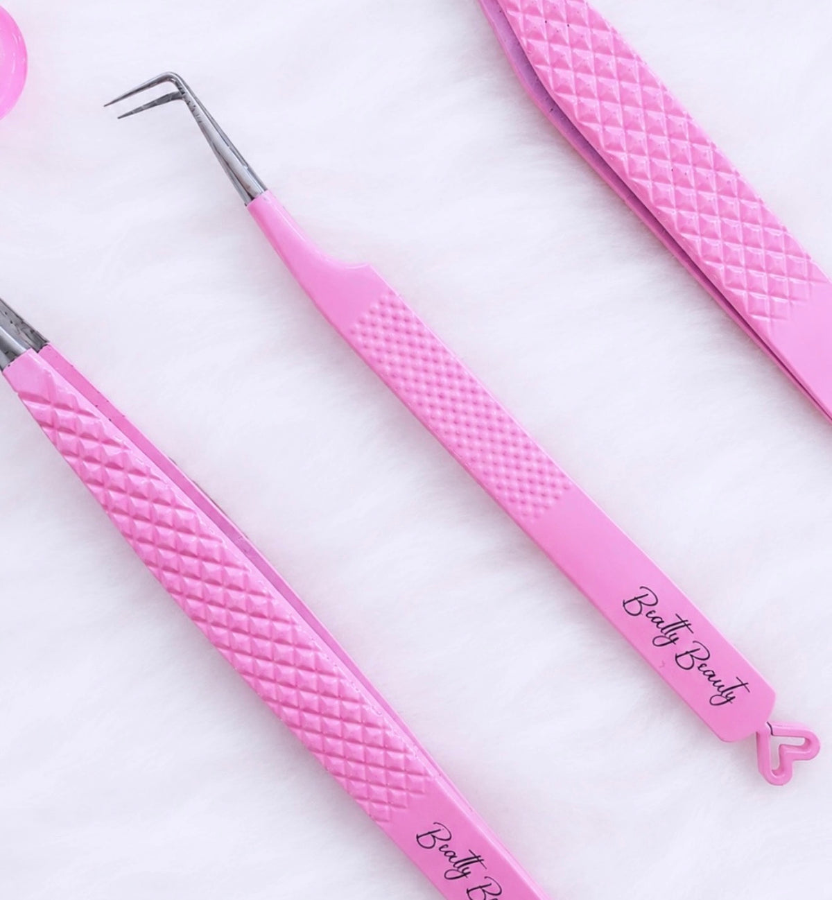 Pink diamond-textured tweezers and spatula tools with silver metal tips, featuring the 'Bath Beauty' brand name printed on the handles, arranged on a white textured background.Tweezer Trio Set lash volume classic tweezers isolation tweezer