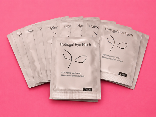 Five silver foil packets of Hydrogel Eye Patch arranged in a fan shape on a solid pink background.100 pairs Of Hydrogel Under Eye Patches Bratty Beauty XO