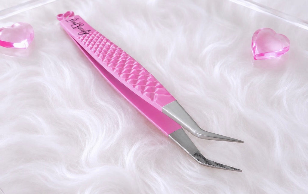 Pink and silver precision tweezers with a textured pink handle, displayed on a white faux fur surface with pink heart-shaped props.Boss Isolation Tweezer bratty beauty xo volume lash tweezer