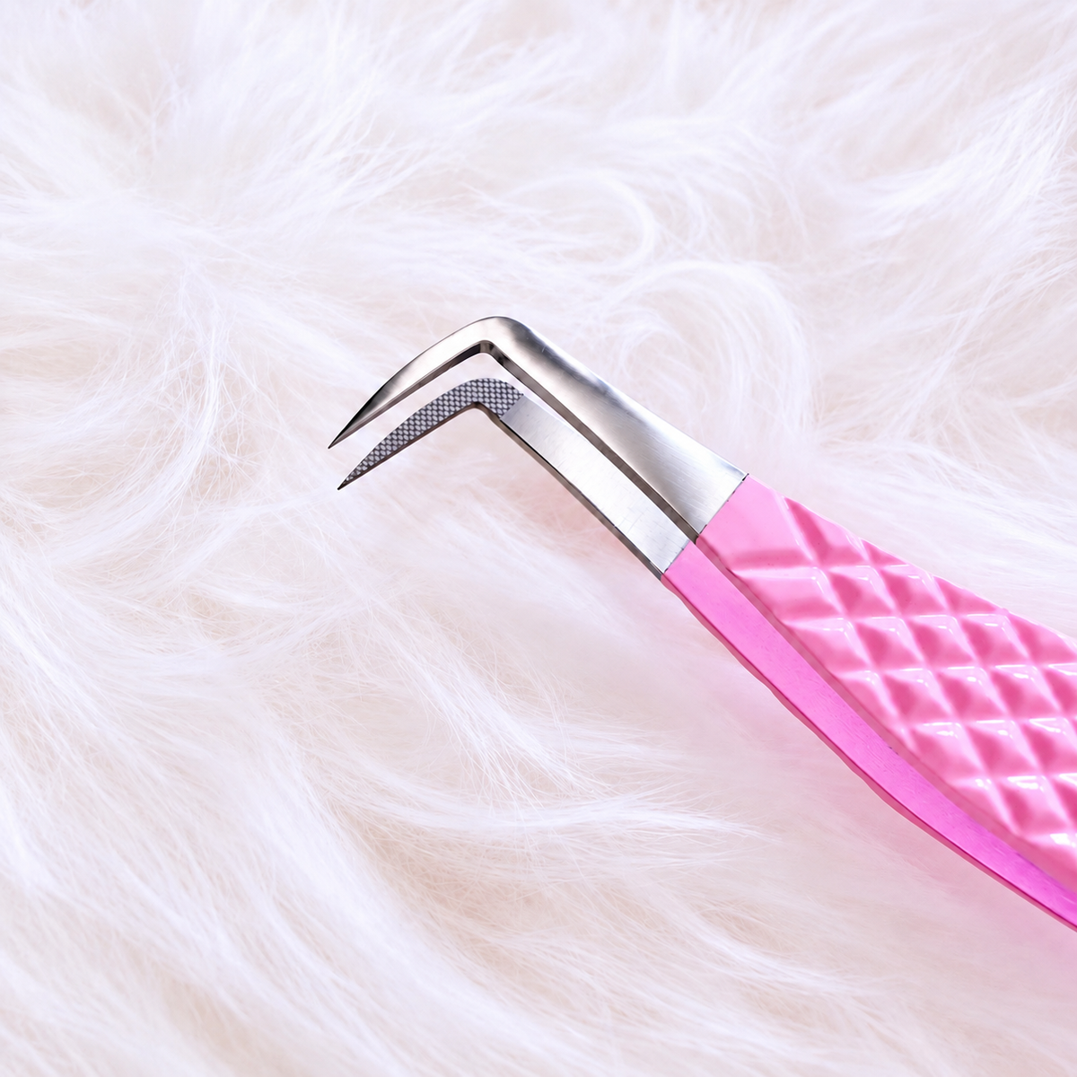 A close-up of a pink and silver curved nail tool with a textured diamond-patterned handle, resting on a soft white faux fur background.Big Boss Fanning Tweezer, bratty beauty xo volume lash tweezer