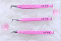 Three pink beauty tweezers with textured grips and silver metal tips, displayed inside a clear acrylic case on a white faux fur background. The tweezers are branded with 'Brattyy Beauty'.Tweezer Trio Set lash volume classic tweezers isolation tweezer