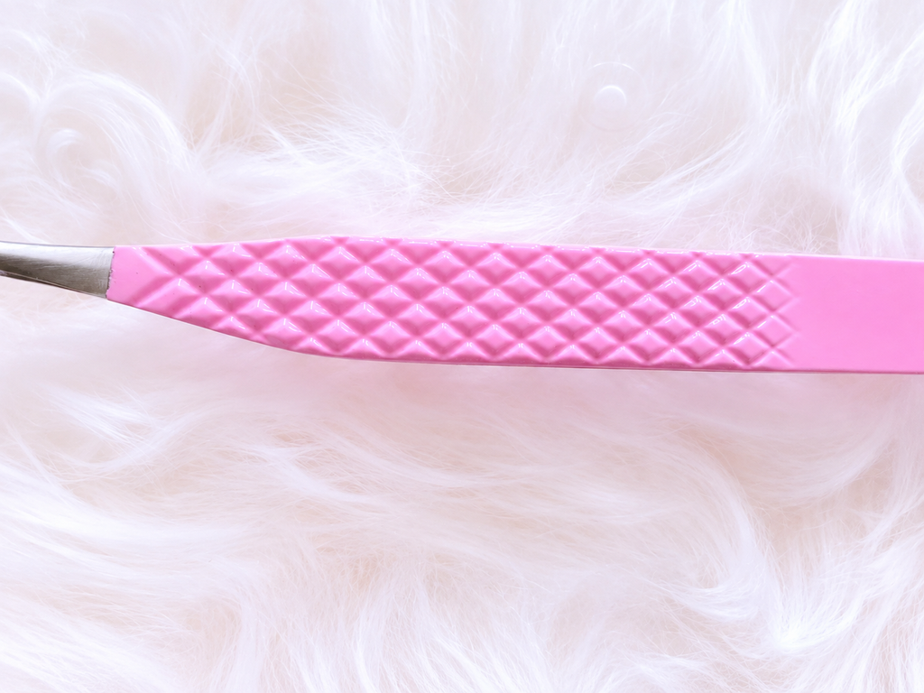 A close-up of a pink silicone tool handle with a diamond-textured grip and a silver metal tip, resting on a white faux fur background.Big Boss Fanning Tweezer, bratty beauty xo volume lash tweezer