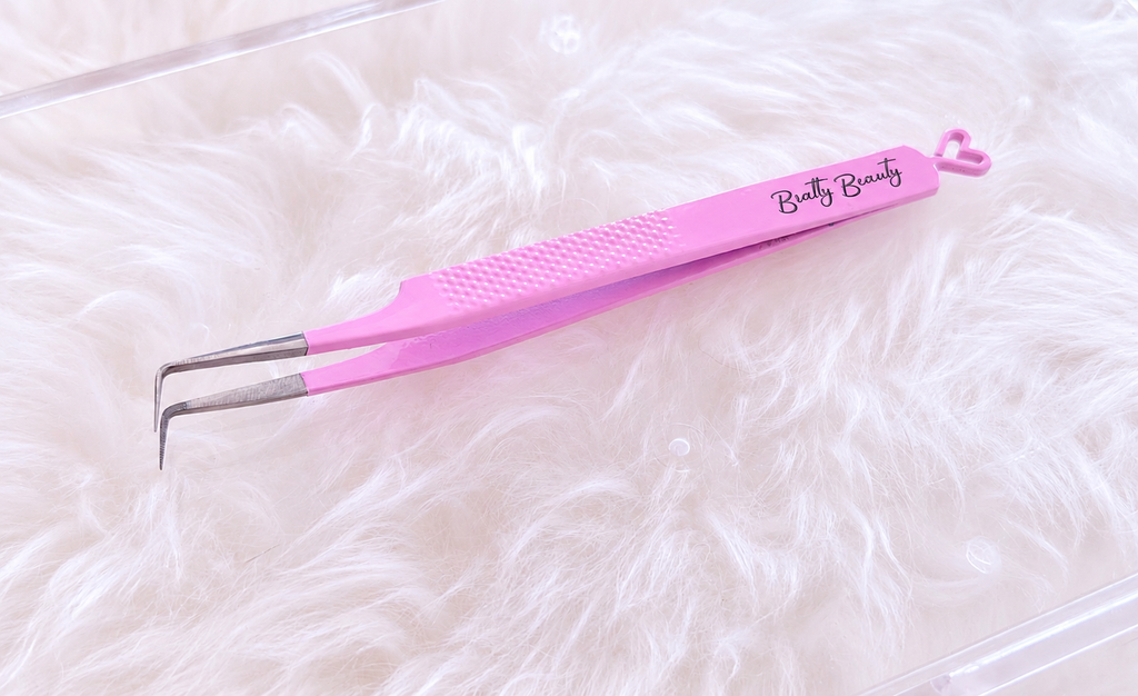 Pink precision tweezers with silver metal tips and a textured grip handle, featuring the 'Butty Beauty' brand name printed on the handle, resting on a white faux fur surface.Boss Babe Fanning Tweezer bratty beauty xo volume lash tweezer 