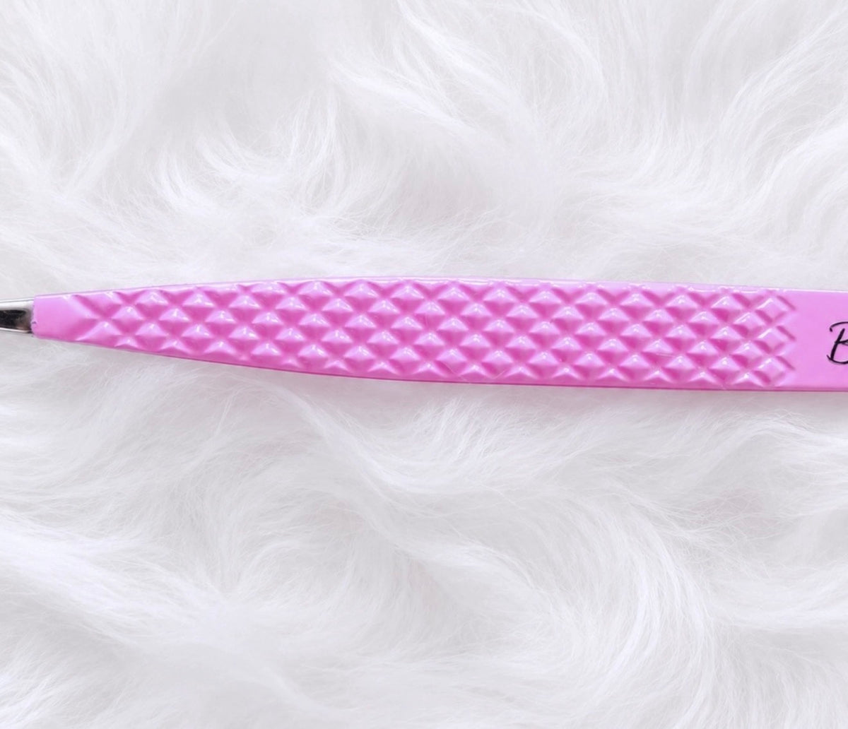 A close-up of a pink textured tool, likely a beauty or grooming device, resting on a white faux fur background.Boss Isolation Tweezer bratty beauty xo volume lash tweezer