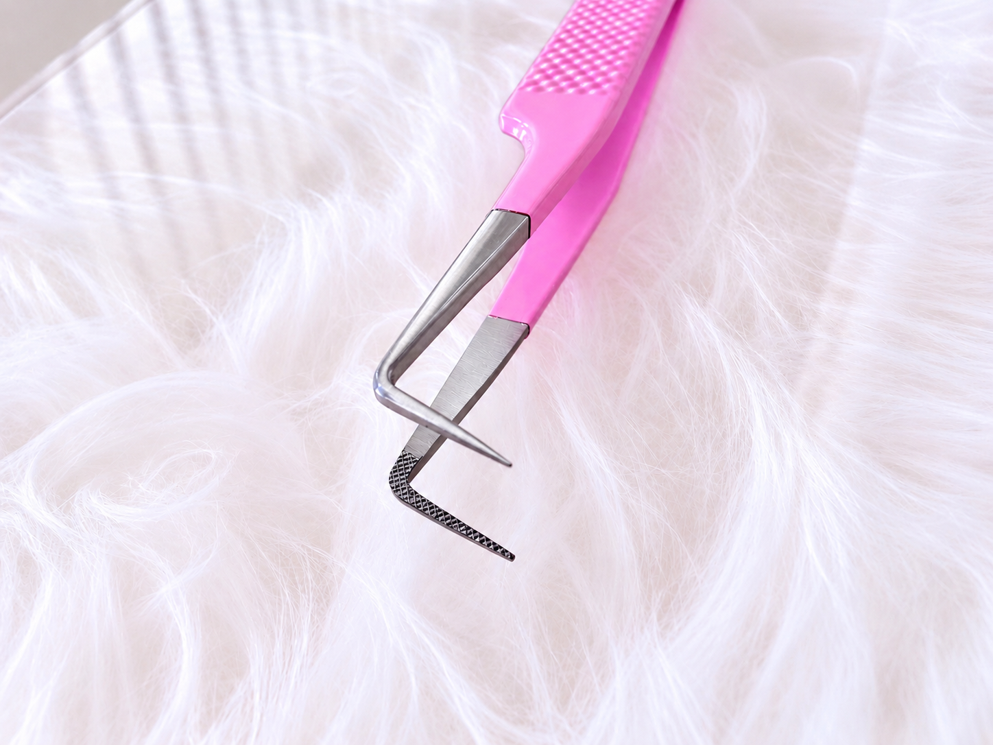 A close-up of a pink-handled metal eyelash extension tool resting on white faux fur.Boss Babe Fanning Tweezer bratty beauty xo volume lash tweezer 