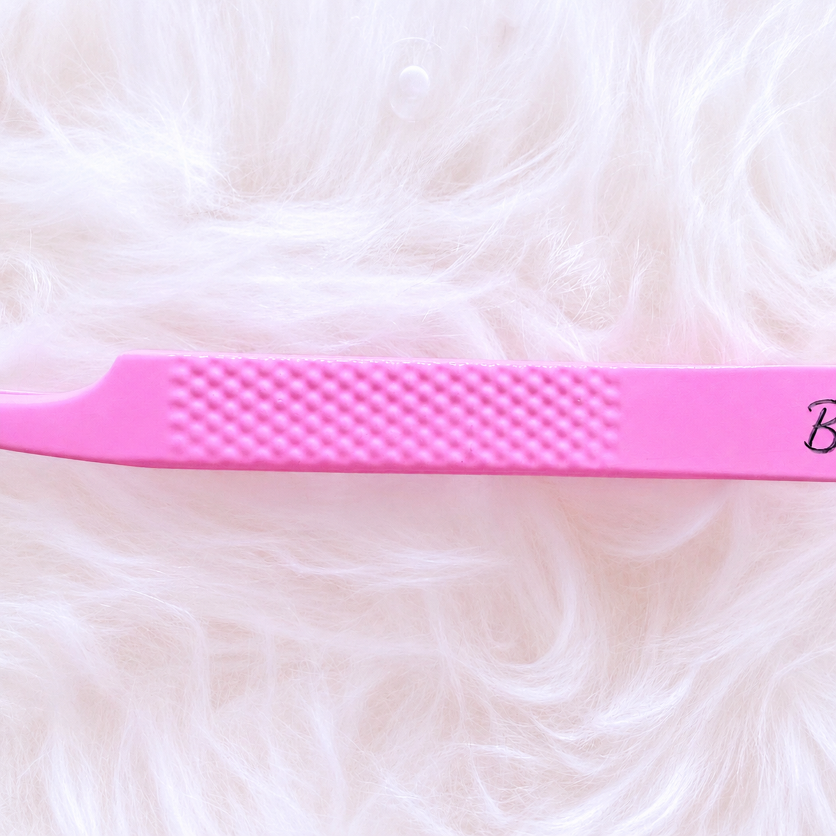 A close-up of a bright pink plastic tool, likely a lash or eyebrow extension tool, resting horizontally on a soft, fluffy white faux fur background.Boss Babe Fanning Tweezer bratty beauty xo volume lash tweezer 
