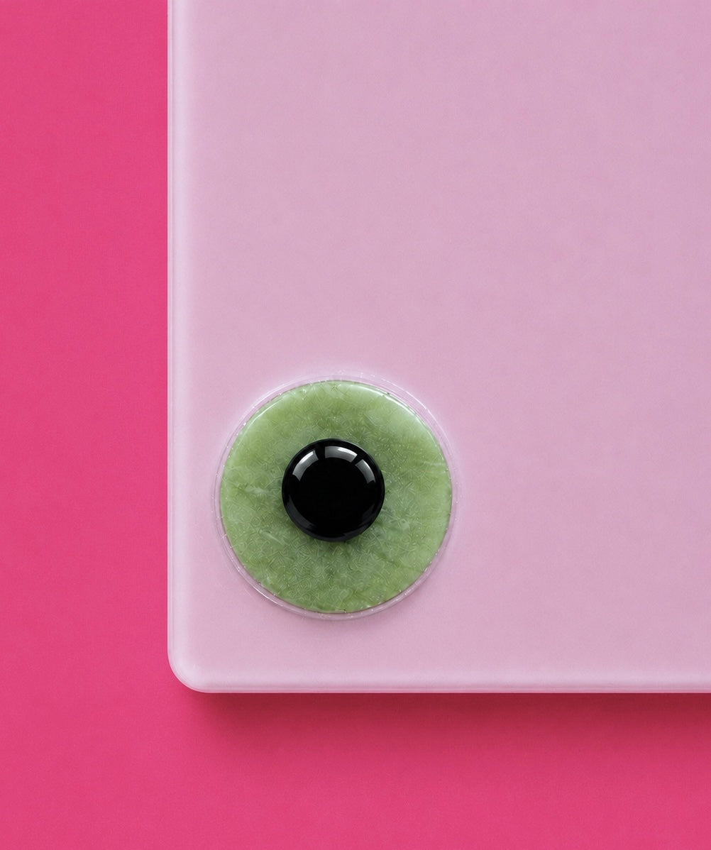 A close-up of a light pink rectangular product corner with a circular green and black lash adhesive glue attached near the bottom edge, set against a solid pink background.Rosie Pink Acrylic Lash Tile Bratty Beauty XO