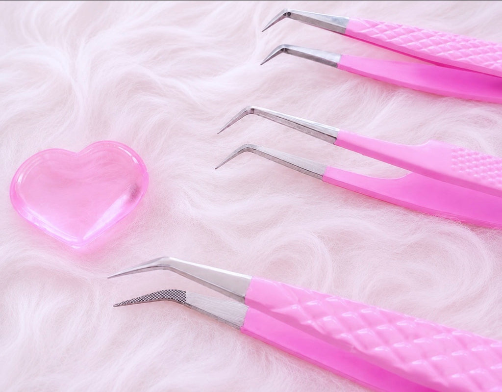 Four pink-handled precision tweezers with silver metal tips arranged on a fluffy white surface next to a translucent pink heart-shaped object.Tweezer Trio Set lash volume classic tweezers isolation tweezer