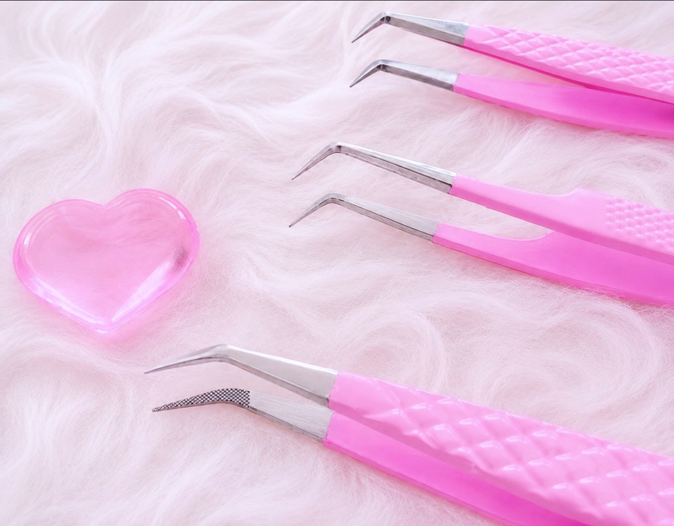Four pink-handled precision tweezers with silver metal tips arranged on a fluffy white surface next to a translucent pink heart-shaped object.Tweezer Trio Set lash volume classic tweezers isolation tweezer