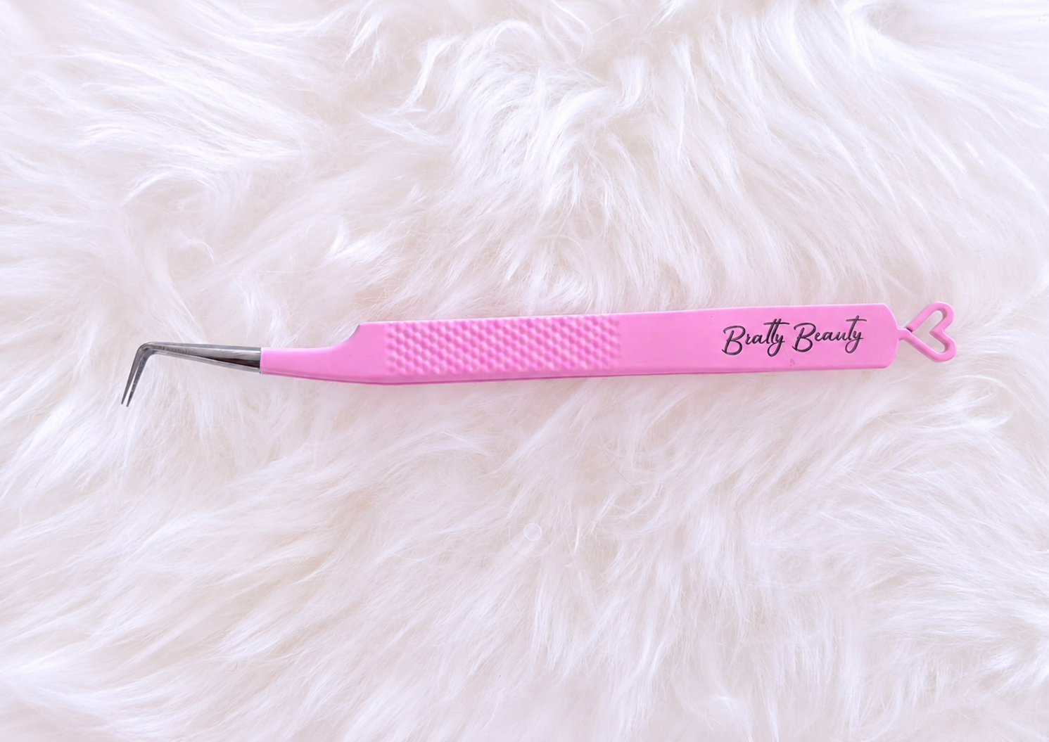 Pink and silver curved beauty tweezers with a textured grip and the brand name 'Butty Beauty' printed on the handle, resting on a white faux fur background.Boss Babe Fanning Tweezer bratty beauty xo volume lash tweezer 